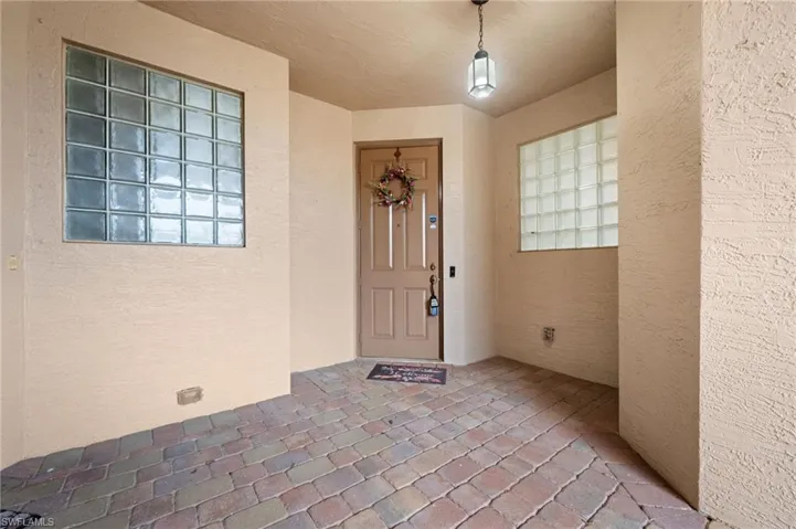 Covered entry with multi-tone paver flooring, textured stucco walls, glass block windows, and a hanging lantern fixture