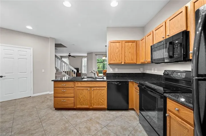 Kitchen featuring wood cabinetry, black appliances, dark countertops, and tile flooring