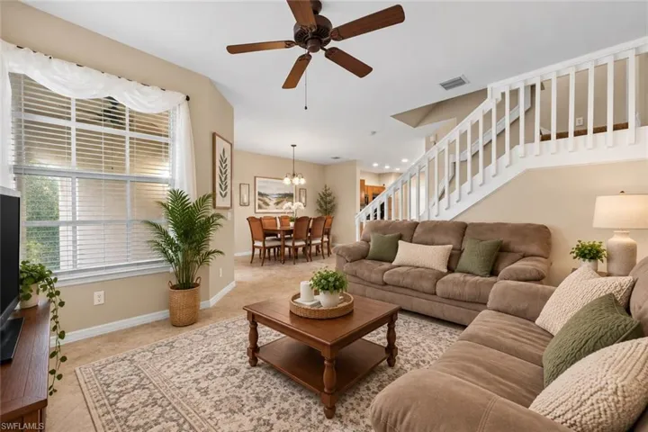 Open-concept living area featuring a prominent window with blinds, a ceiling fan, and a staircase with white balusters