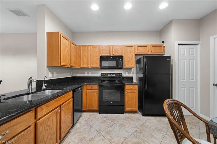 Kitchen with wood cabinetry, dark countertops, black appliances, and tiled flooring