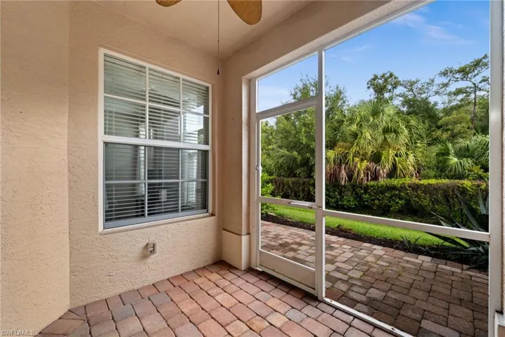 Screened patio with brick paver flooring, textured stucco wall, and a window with horizontal blinds