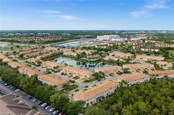 Community featuring multiple residential structures, a central pond, and ample parking, surrounded by mature trees