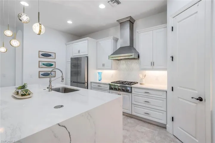Kitchen featuring wall chimney range hood, stainless steel appliances, decorative backsplash, sink, and light stone counters