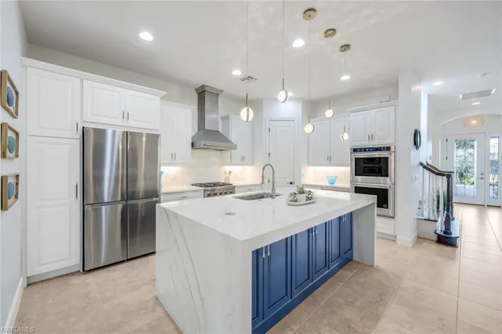 Kitchen with white cabinets, stainless steel appliances, wall chimney exhaust hood, decorative backsplash, and sink