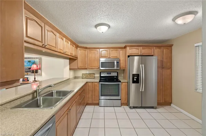 Kitchen with appliances with stainless steel finishes, a sink, light countertops, a textured ceiling, and light tile patterned floors