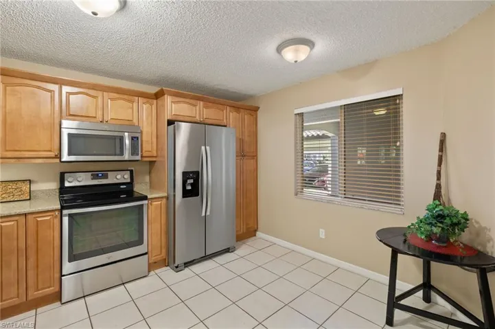 Kitchen with appliances with stainless steel finishes, a textured ceiling, baseboards, and light stone countertops