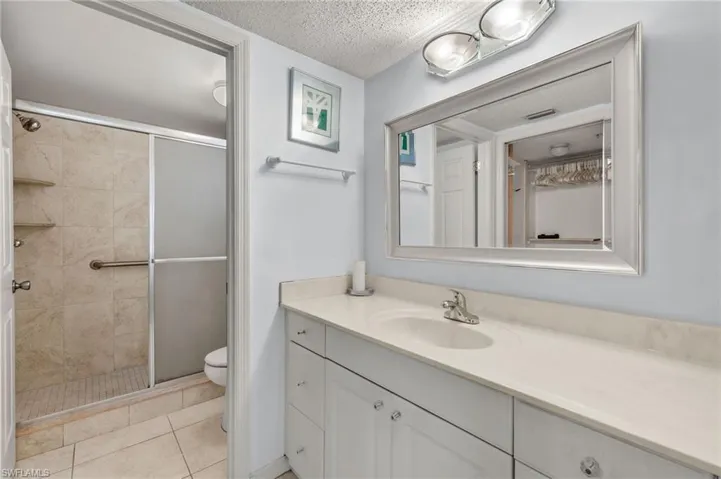 Full bath featuring a textured ceiling, a shower stall, toilet, vanity, and tile patterned floors