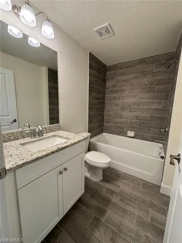 Bathroom featuring a white vanity with a light-colored countertop, recessed sink with chrome faucet, shower-tub combination with horizontal tile surround, and wood-finish tile flooring