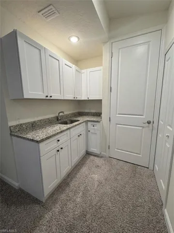 Compact kitchen area featuring a stainless steel sink, granite countertops, white cabinetry with dark hardware, and recessed lighting