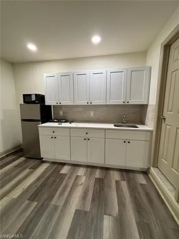 White shaker-style cabinetry with dark hardware, light countertop, stainless steel sink, and wood-finish flooring