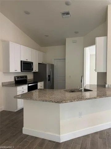 Kitchen featuring a vaulted ceiling, recessed lighting, white cabinetry, a built-in microwave, and a breakfast bar with an undermount sink