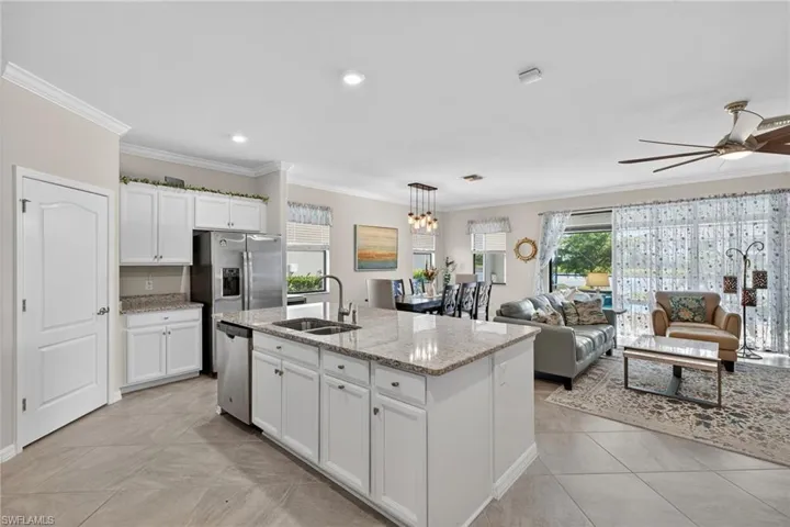 Kitchen with white cabinetry, decorative light fixtures, crown molding, light stone countertops, and plenty of natural light