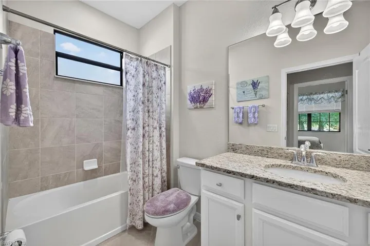 Bathroom featuring healthy amount of natural light, vanity, shower / tub combo with curtain, and light tile patterned flooring