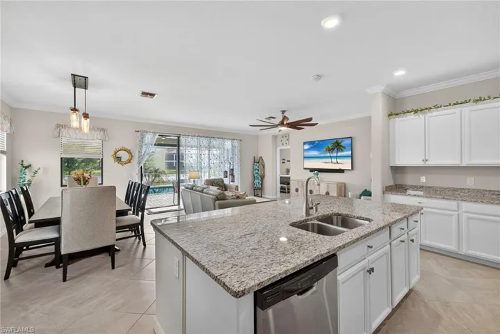 Kitchen featuring white cabinets, a kitchen island with sink, crown molding, stainless steel dishwasher, and light stone counters