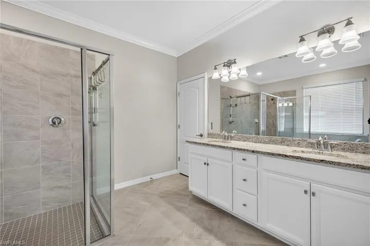 Full bathroom featuring double vanity, ornamental molding, and a shower stall