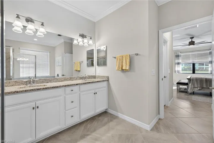 Ensuite bathroom featuring double vanity, crown molding, a ceiling fan, light tile patterned floors, and an enclosed shower