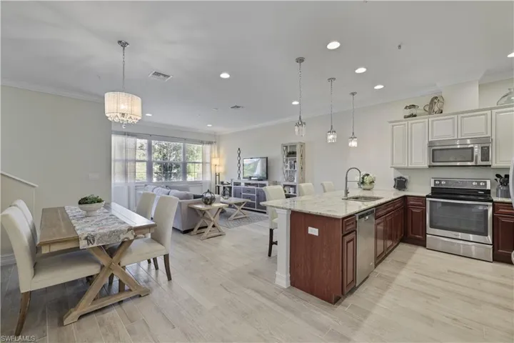 Kitchen featuring a kitchen breakfast bar, appliances with stainless steel finishes, decorative light fixtures, a peninsula, and crown molding