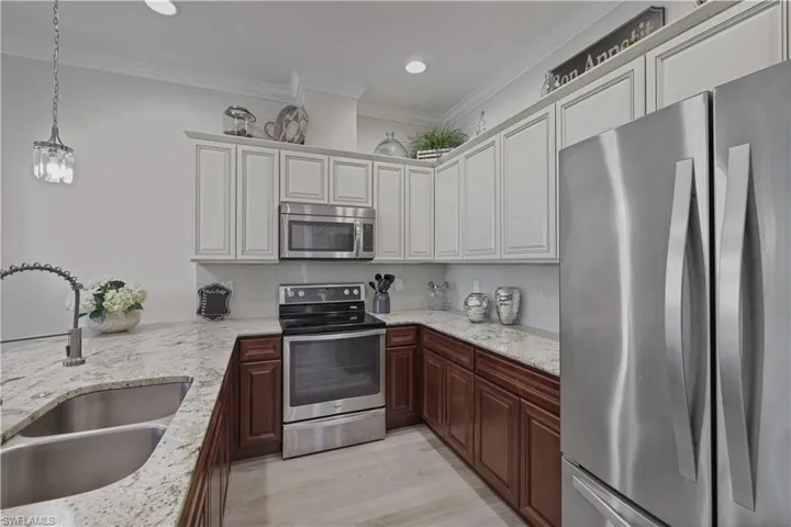 Kitchen featuring stainless steel appliances, crown molding, decorative light fixtures, light stone countertops, and backsplash