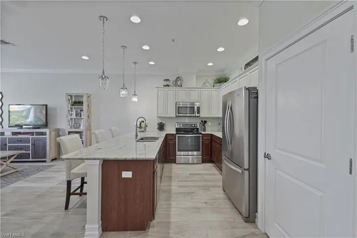 Kitchen with a breakfast bar, ornamental molding, stainless steel appliances, a peninsula, and pendant lighting