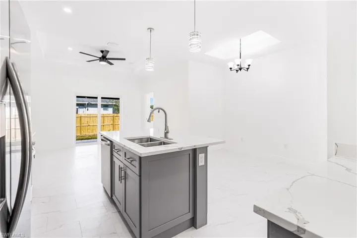 Kitchen with gray cabinetry, stainless steel appliances, sink, pendant lighting, and an island with sink