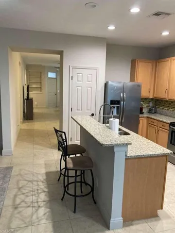 Kitchen featuring a granite-topped island with breakfast bar seating, light wood-finish cabinetry, stainless steel appliances, and tile flooring
