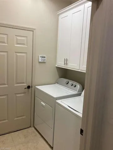 Laundry area with overhead white cabinetry, tile flooring, and a paneled door with dark hardware