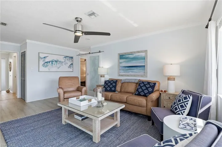 Living room featuring a barn door, ornamental molding, ceiling fan, and wood finished floors
