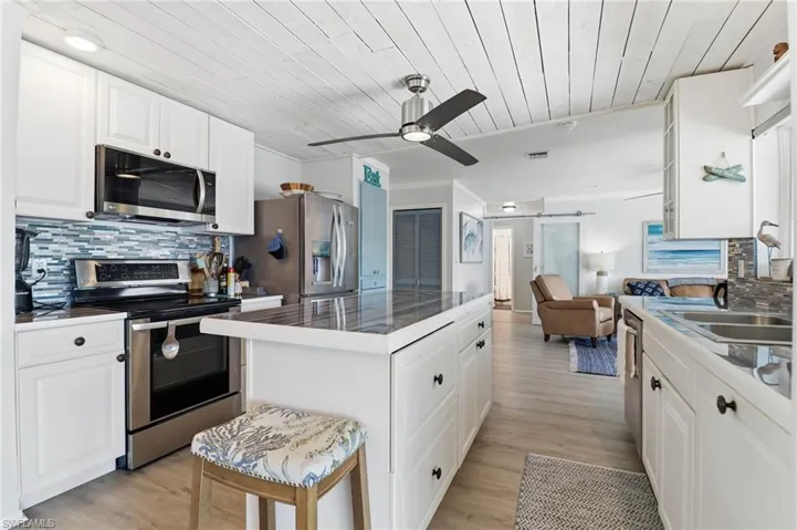 Kitchen featuring decorative backsplash, white cabinets, stainless steel appliances, wood ceiling, and a barn door