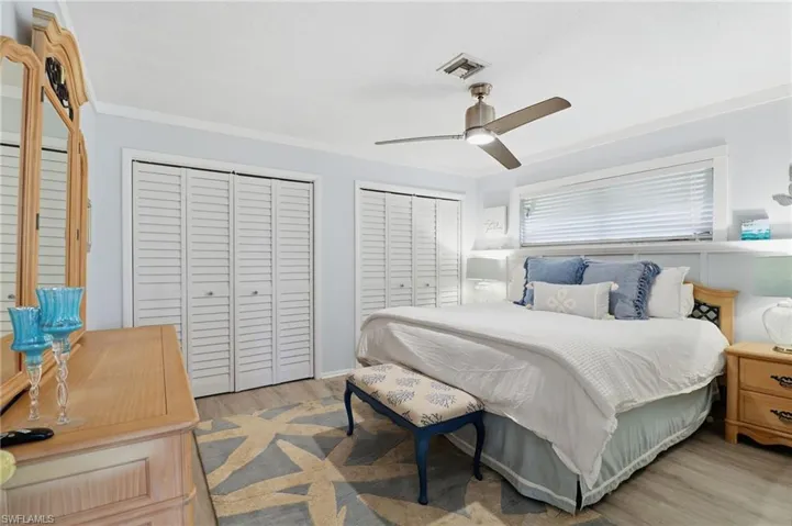 Bedroom with two closets, ceiling fan, light wood-style floors, and crown molding