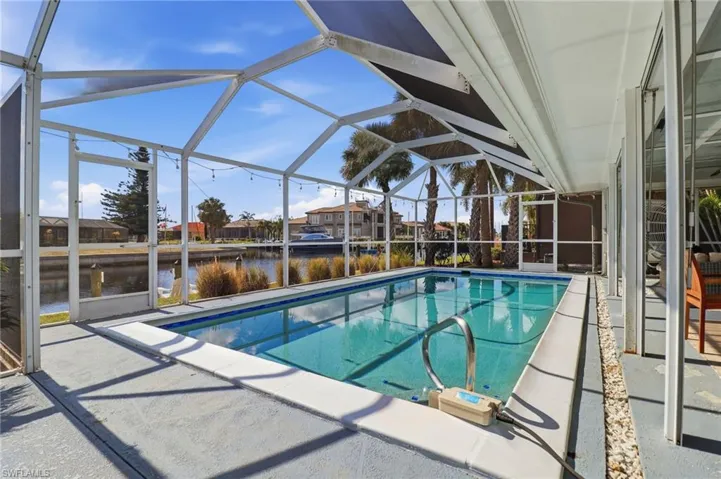 Outdoor pool featuring a sunroom, a patio, glass enclosure, and a water view