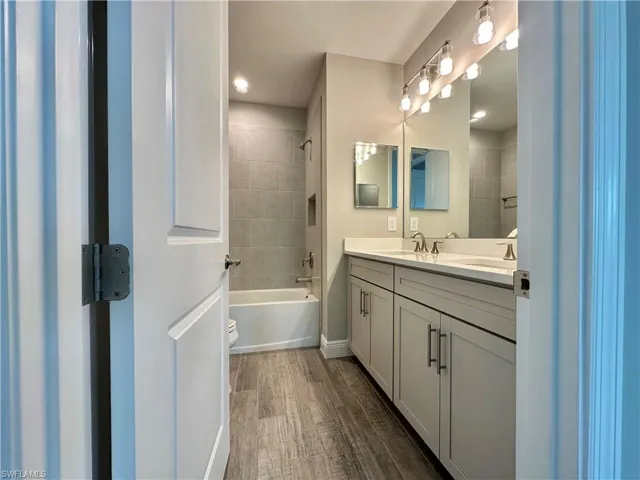 Bathroom with double vanity, dark wood-style floors, and shower / washtub combination