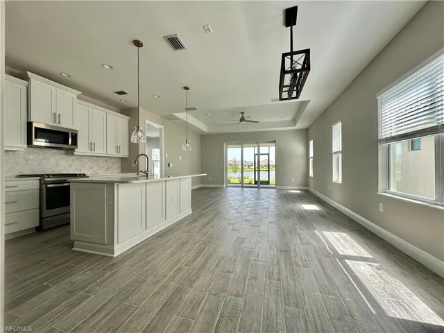 Kitchen featuring a raised ceiling, white cabinets, stainless steel appliances, hanging light fixtures, and open floor plan