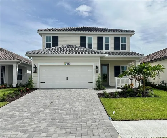 View of front of property featuring a tiled roof, an attached garage, decorative driveway, a front lawn, and a porch
