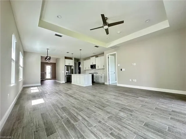 Unfurnished living room featuring a ceiling fan, wood tiled floors, a tray ceiling, and recessed lighting