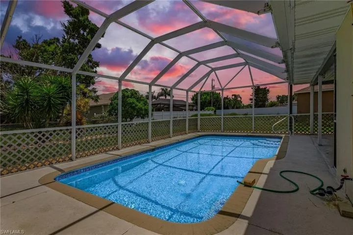 Pool at dusk featuring glass enclosure and a patio area