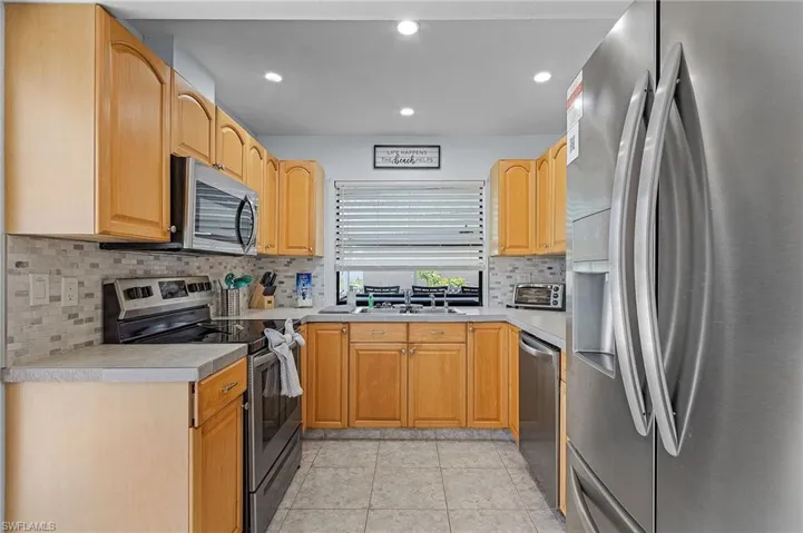 Kitchen with decorative backsplash, sink, light tile patterned flooring, and stainless steel appliances