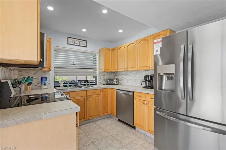 Kitchen featuring sink, light brown cabinets, tasteful backsplash, light tile patterned floors, and appliances with stainless steel finishes
