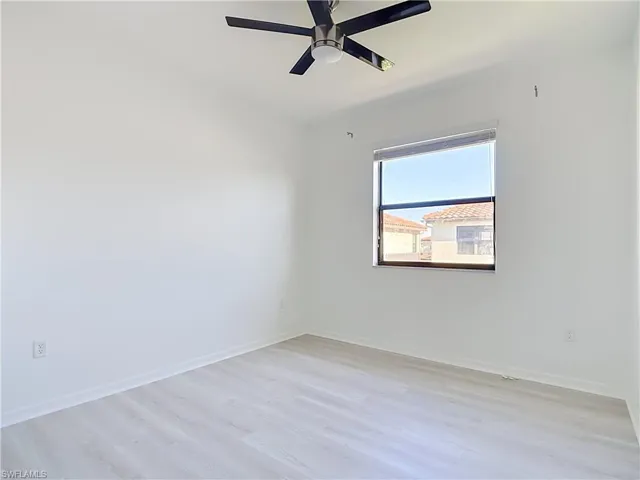Room featuring light-toned wood-finish flooring, a window with exterior residential structures visible, and a ceiling fan with integrated lighting