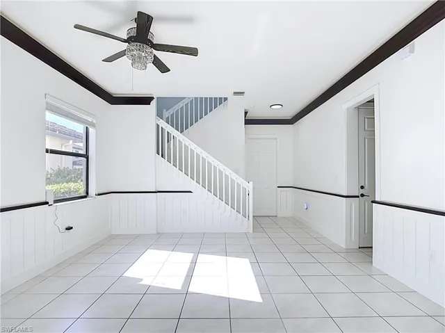 Expansive open-concept room featuring white tile flooring, beadboard wainscoting, and dark crown molding