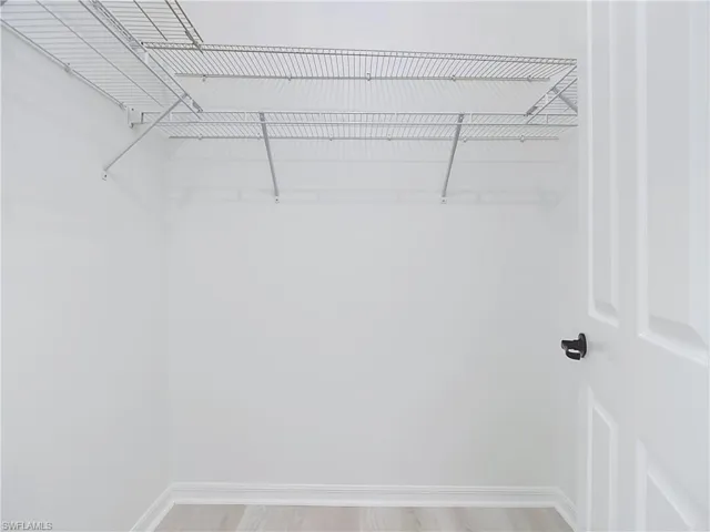 Spacious closet featuring wire shelving, bright white walls, light wood-finish flooring, and white baseboards