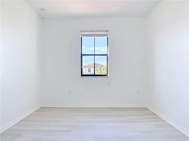 Bright interior space featuring a window with black trim, light wood-finish flooring, white baseboards, and neutral wall tones