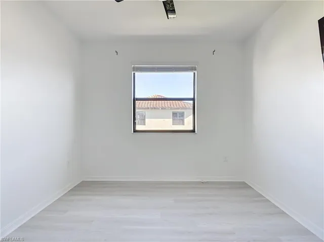 Bright room featuring a window with a dark frame, light wood-finish flooring, and crisp white walls