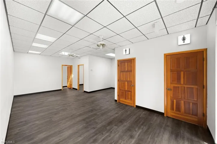 Unfurnished room with ceiling fan, a drop ceiling, and dark wood-type flooring