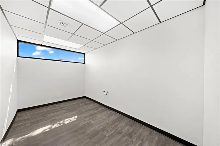 Unfurnished room with dark hardwood / wood-style flooring, expansive windows, and a drop ceiling