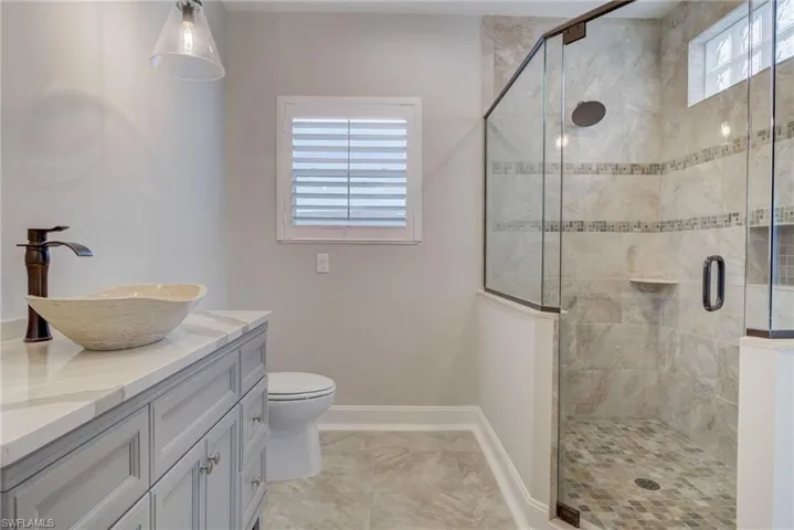 Bathroom with a shower with door, vanity, tile patterned flooring, and toilet