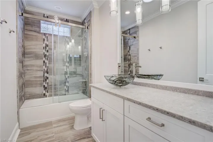 Full bathroom with ornamental molding, vanity, toilet, and combined bath / shower with glass door