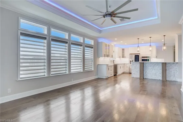 Unfurnished living room featuring ornamental molding, dark hardwood / wood-style floors, ceiling fan, and a tray ceiling