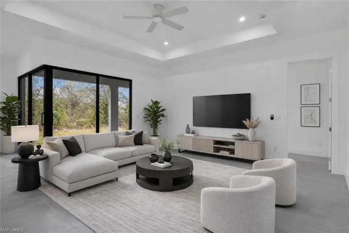 Living area featuring concrete floors, a tray ceiling, ceiling fan, and recessed lighting. This photo is virtually staged.