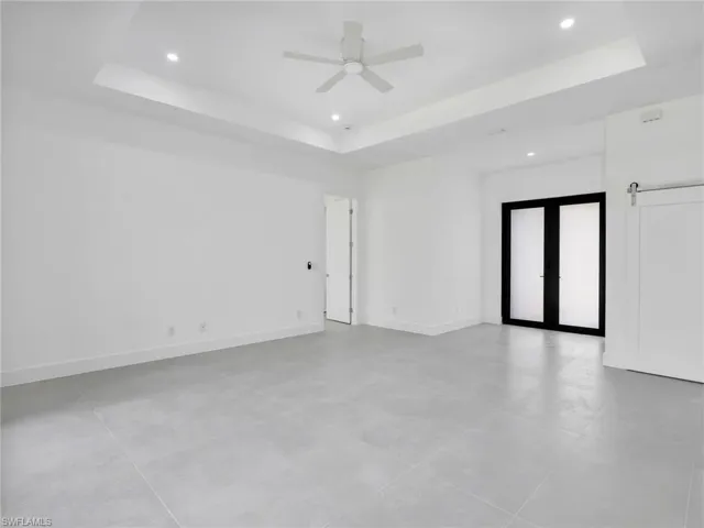 Empty room with french doors, a tray ceiling, ceiling fan, recessed lighting, and a barn door