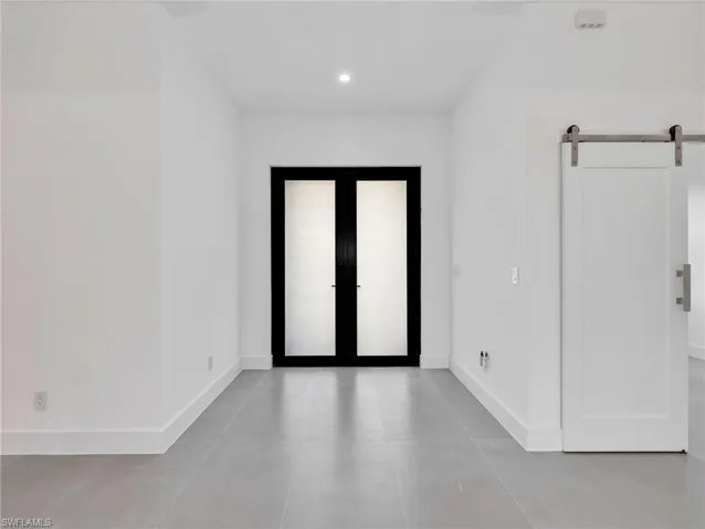 Empty room with a barn door, french doors, and recessed lighting